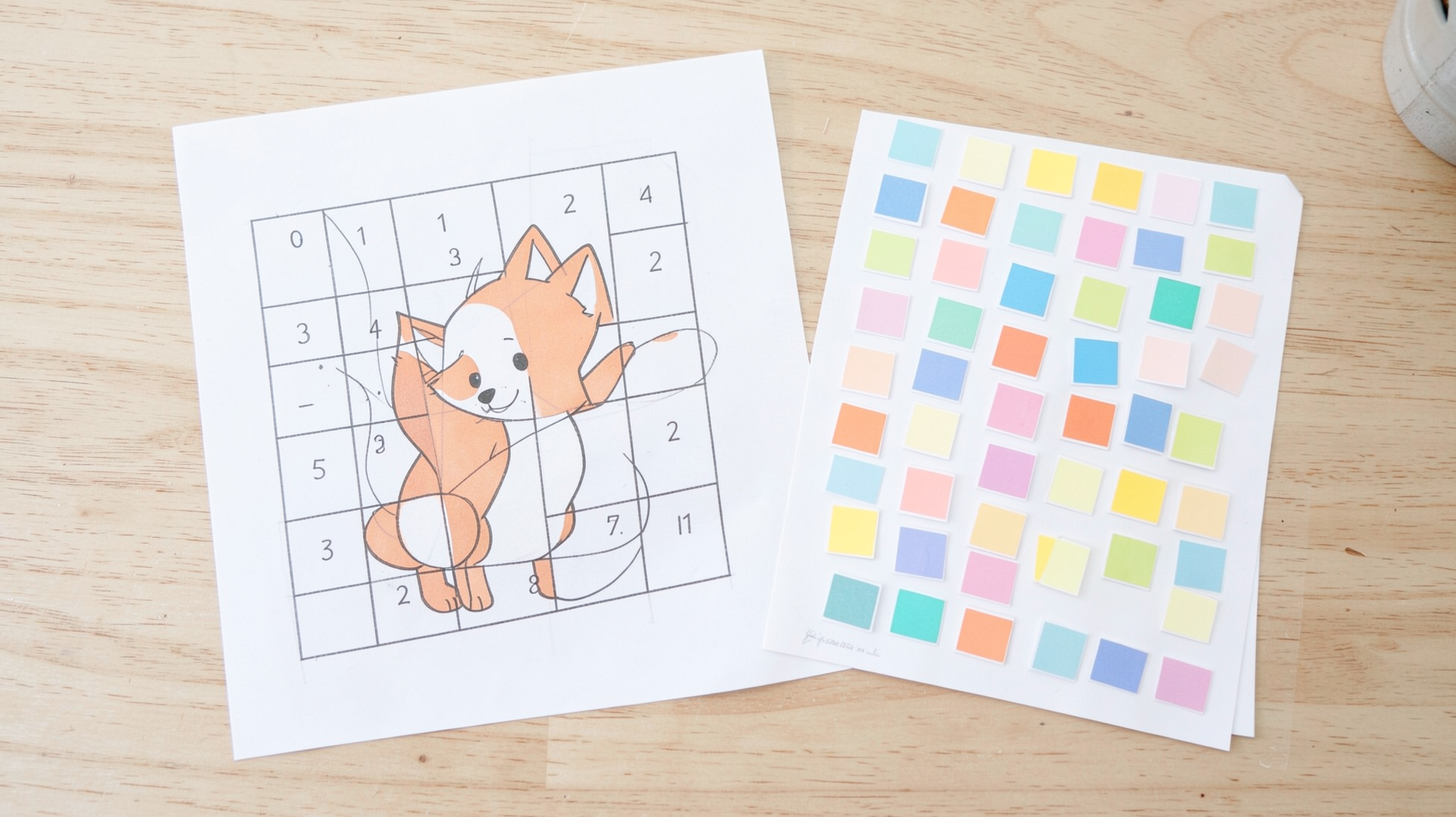 A printed mosaic grid of a cartoon fox beside a printed sheet of small colored square stickers